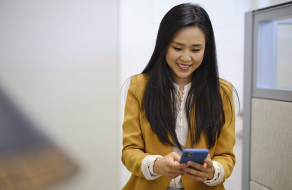A businesswoman in a modern office, sending and receiving text messages on a smartphone
