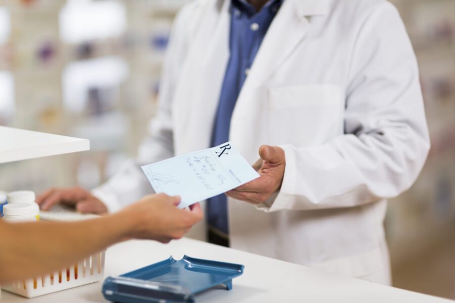 A man handing a handwritten prescription to a pharmacist