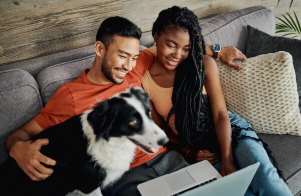 Young couple sitting with their pet dog in their living room at home and using a laptop