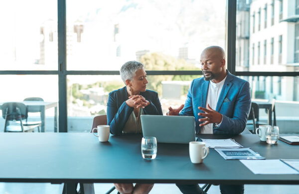 Businessman on a laptop in a modern corporate office collaborating with a female colleague