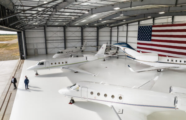 Five private planes parked inside a massive hangar bearing the United States flag