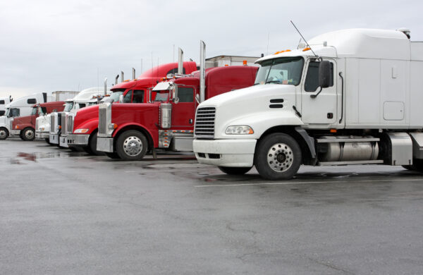 A variety of parked, nondescript semi trucks at a busy interstate truck stop